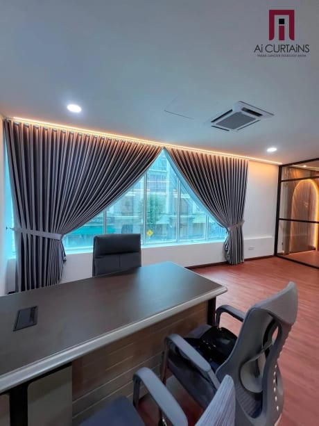 A private office with grey floor-length drapes at the window, a desk and chair, and warm light along a recessed ceiling.
